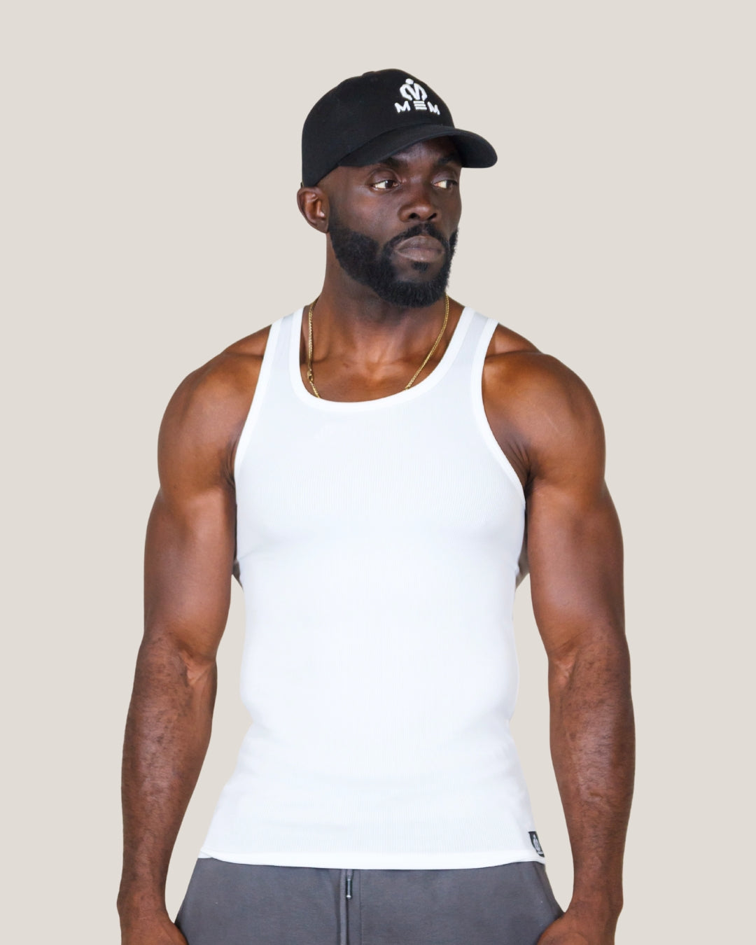 Man wearing a white tank top and black cap against a beige background