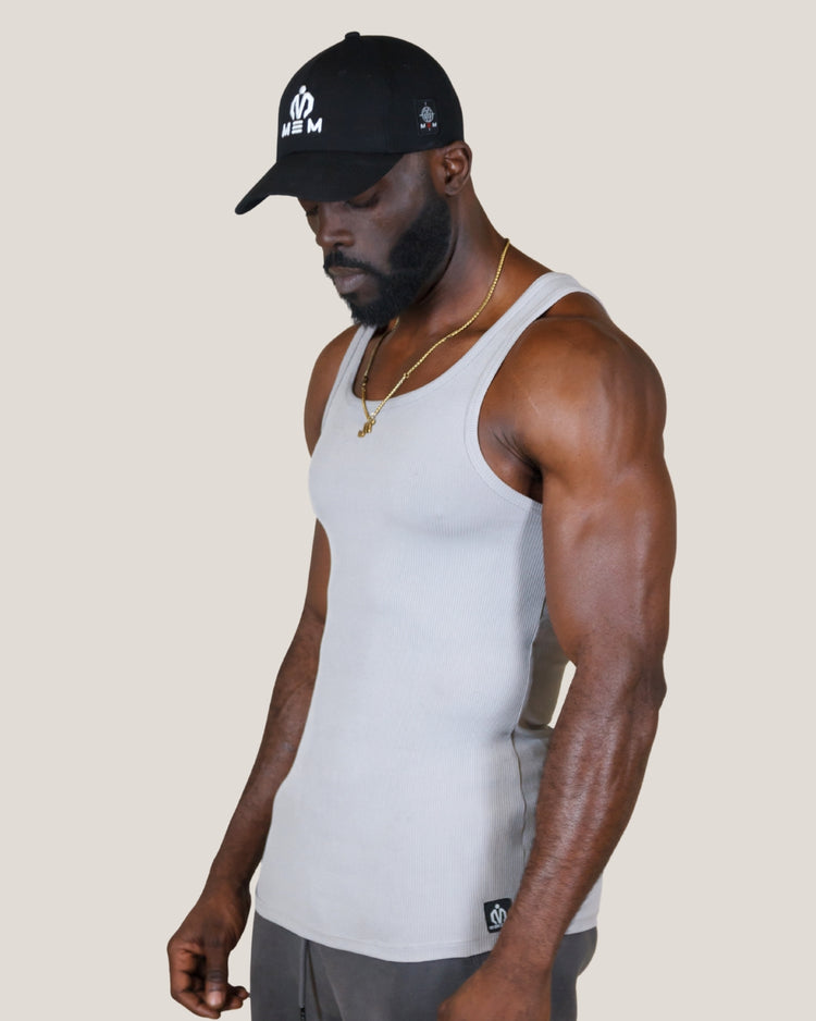 Man wearing a white tank top and black cap with a logo on a beige background