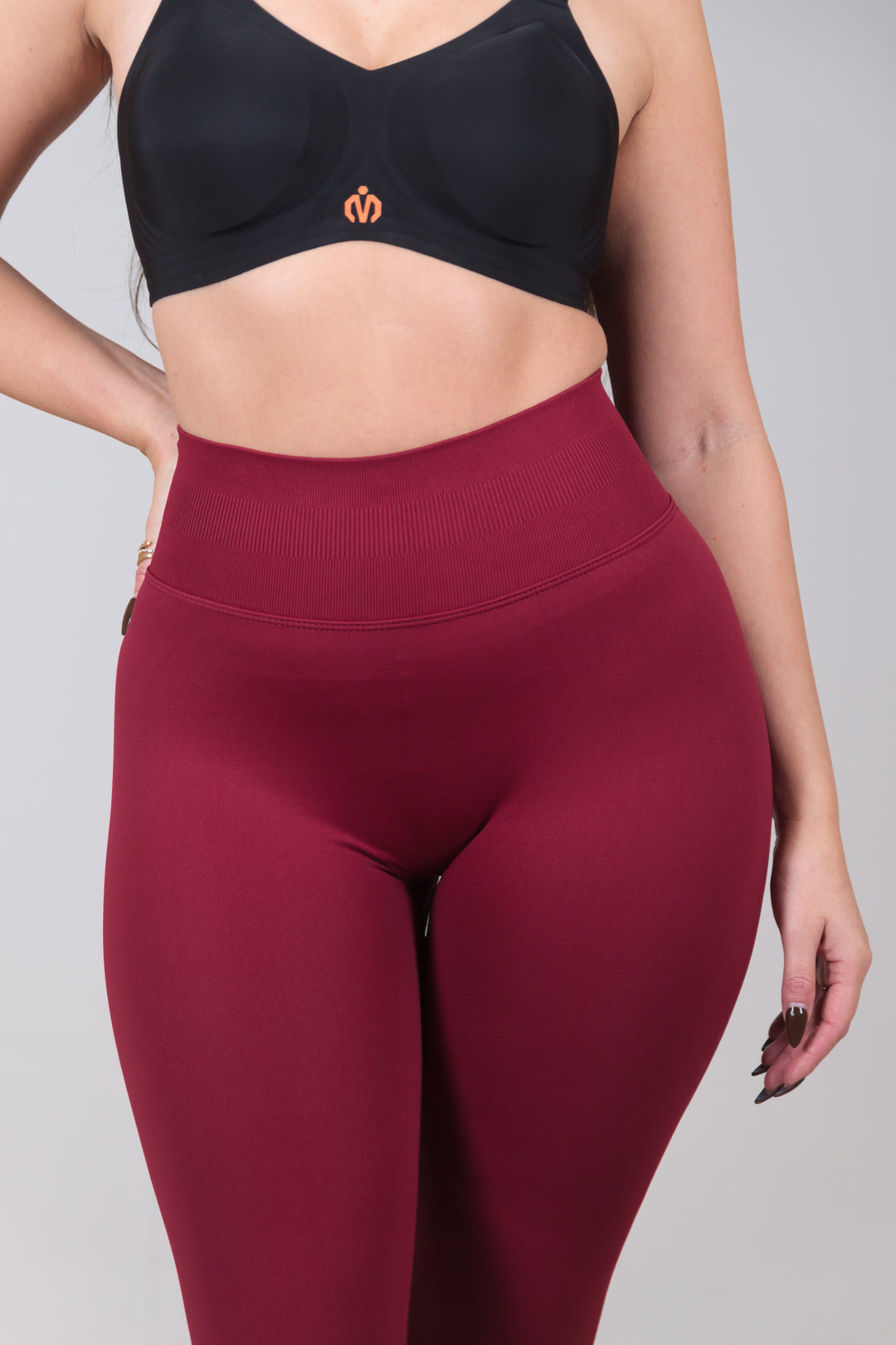 Person wearing a black sports bra and maroon leggings on a gray background