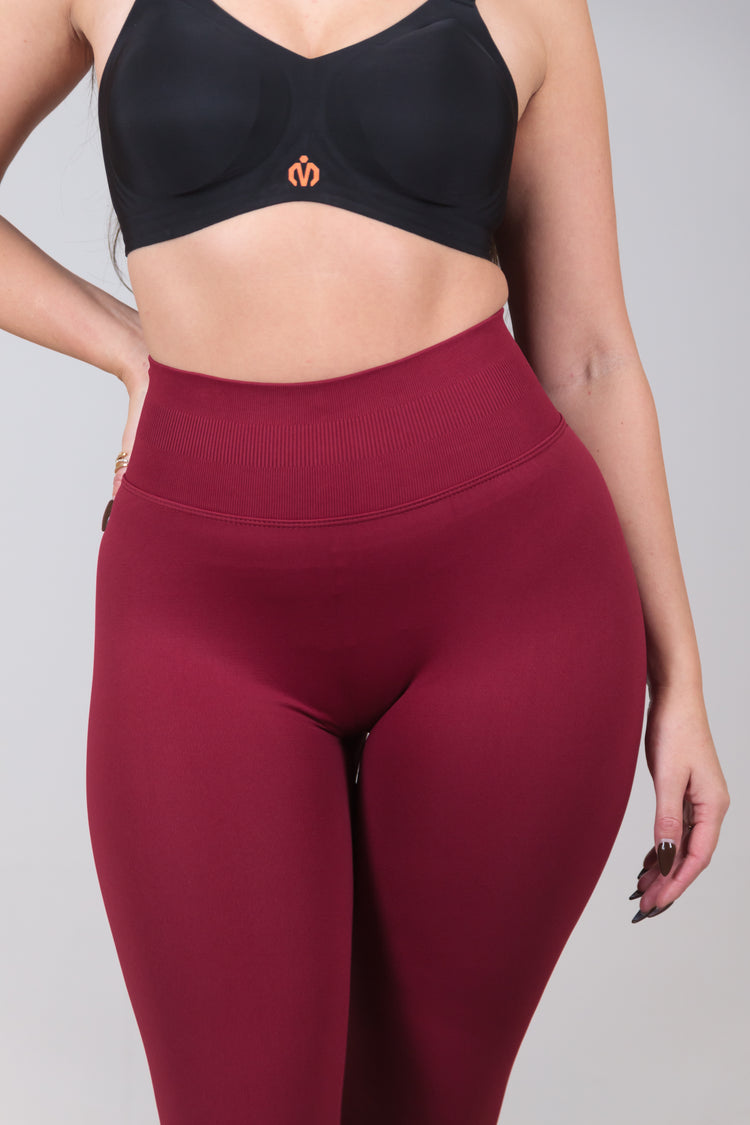 Person wearing a black sports bra and maroon leggings on a gray background