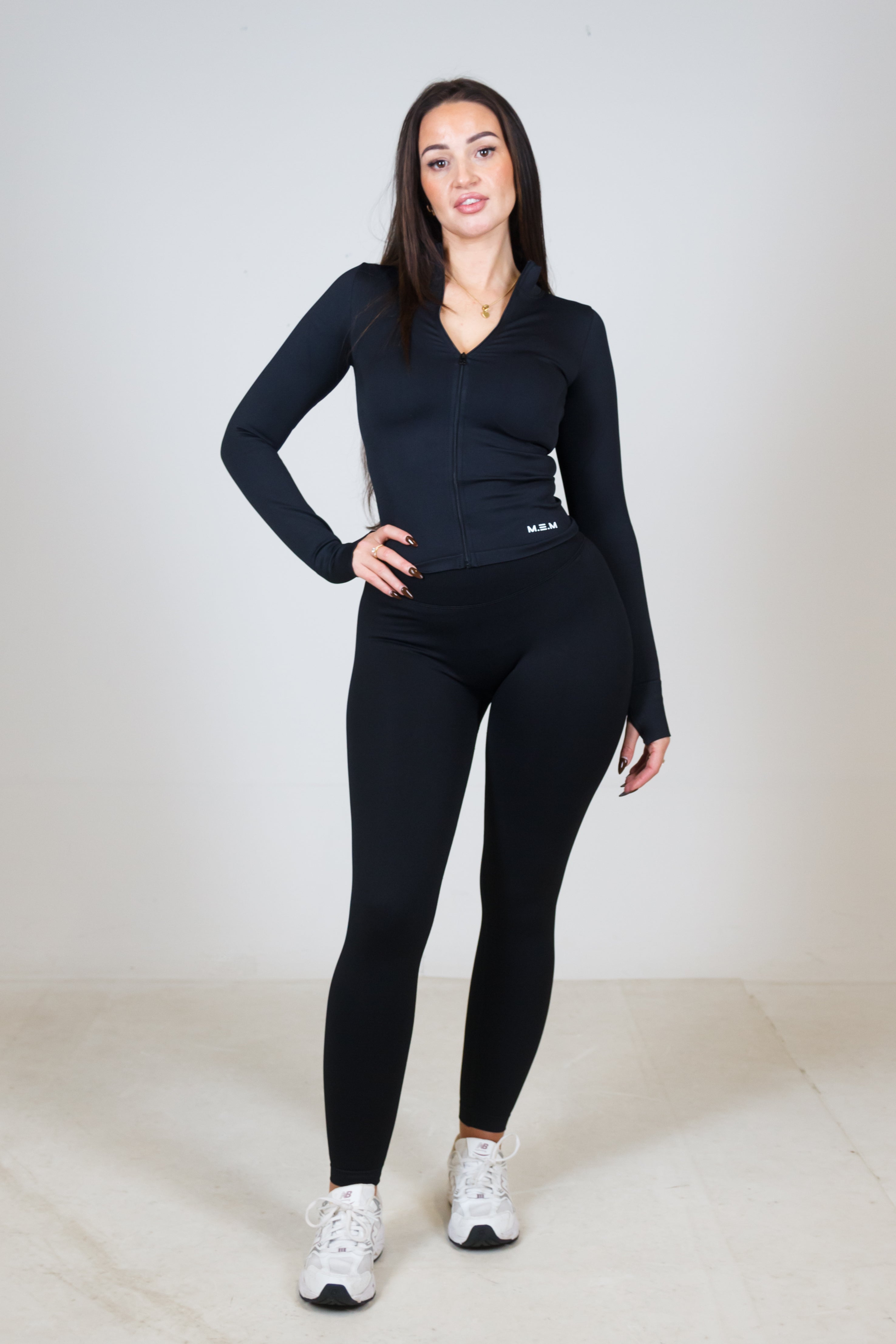 Woman wearing a black long-sleeve top and leggings on a white background