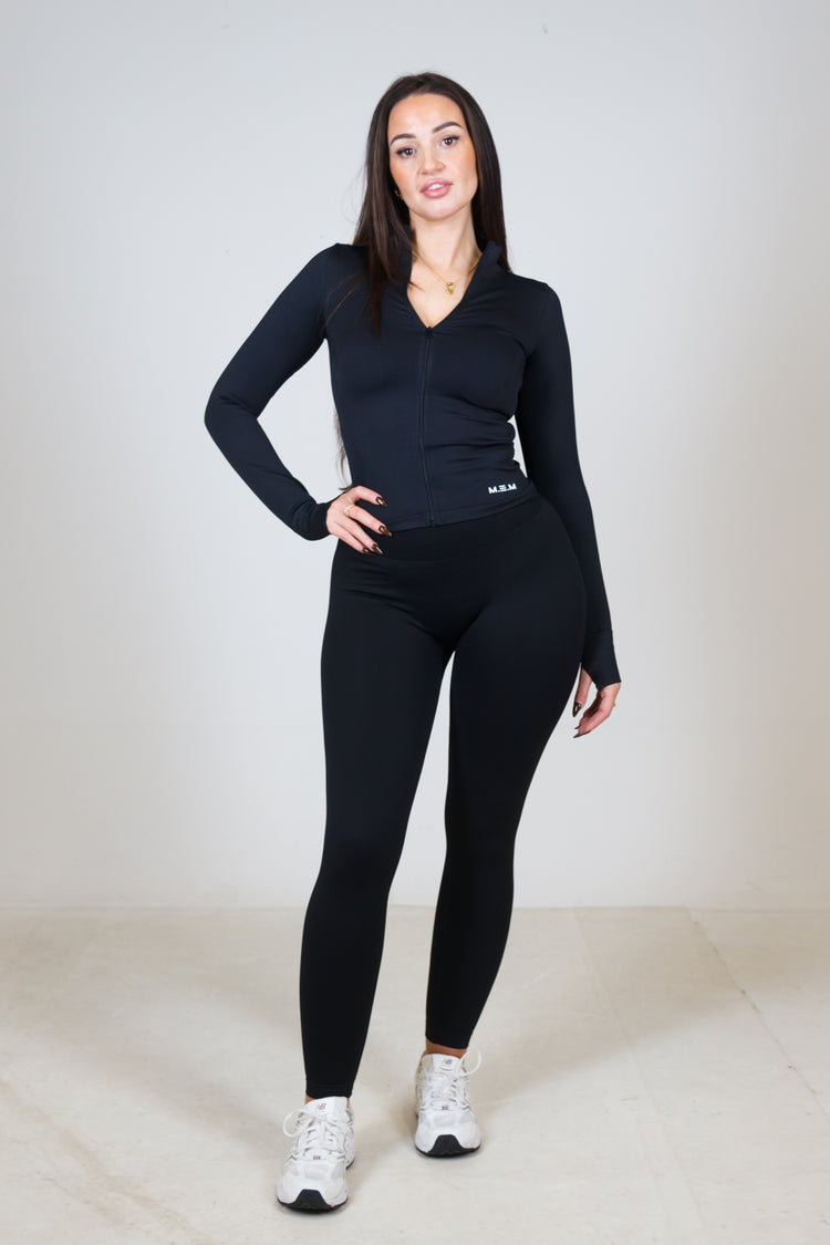 Woman wearing a black long-sleeve top and leggings on a white background