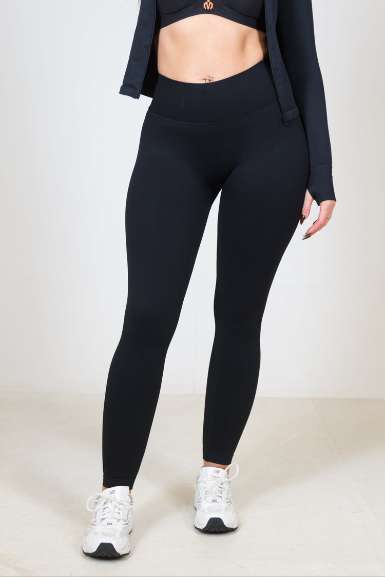 Person wearing black athletic leggings with a matching top and jacket on a white background