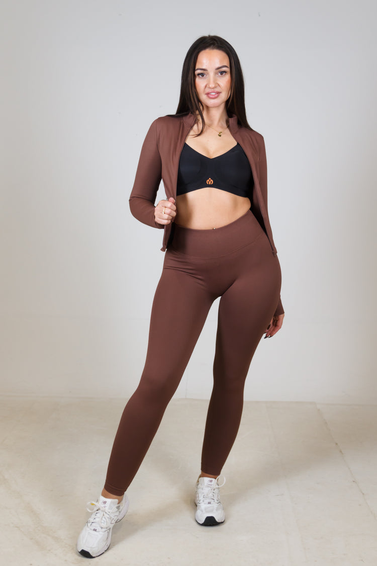 Woman wearing a brown athletic outfit with a black sports bra on a white background