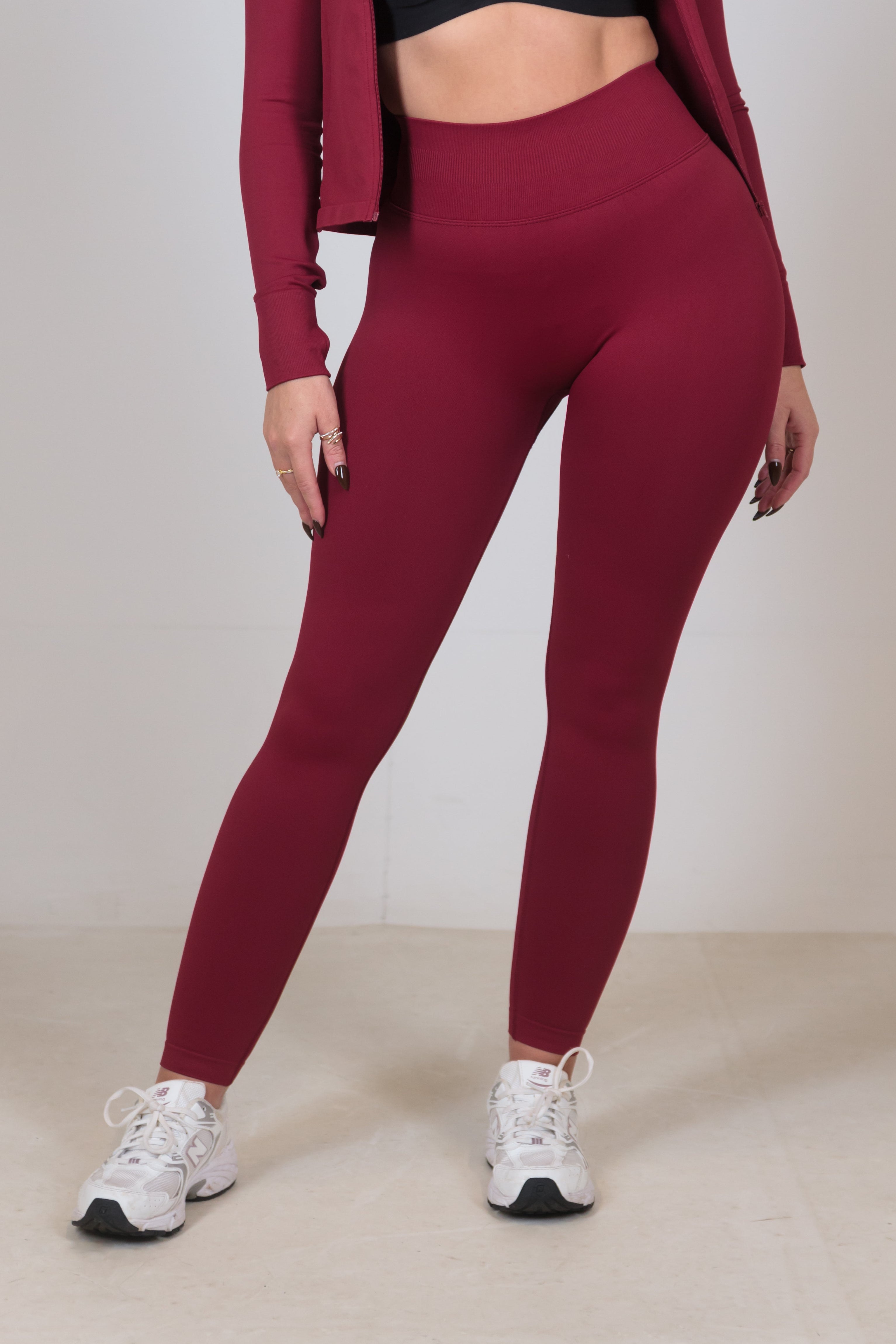 Person wearing maroon leggings, black sports bra, and red jacket on a plain background